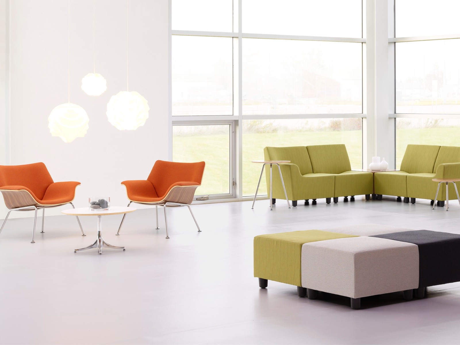 Des chaises longues Orange Swoop et des sièges modulaires Swoop vert dans un espace de réunion décontracté.